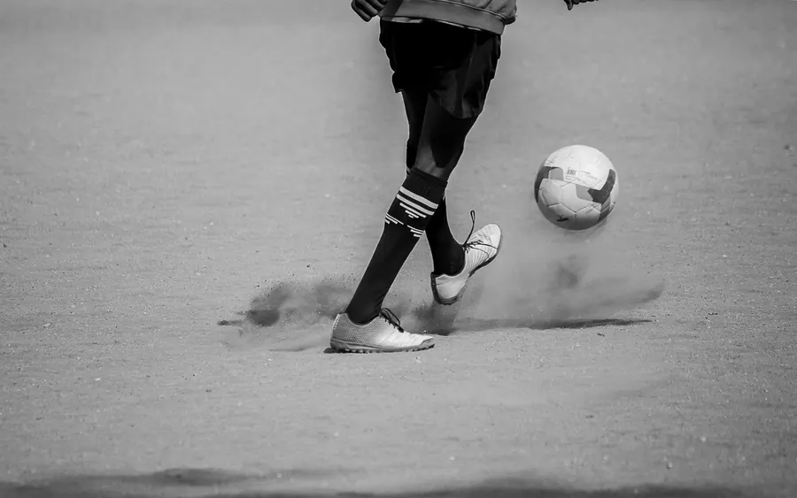 Jugador ejecutando un pase en cancha de tierra, entrenamiento de fútbol